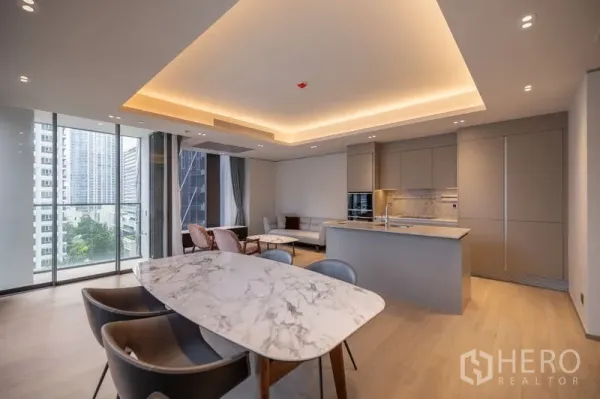 Condominium for rent in Pathum Wan, Bangkok - Open-plan living and dining with a marble table, island kitchen, floor-to-ceiling windows and city view.