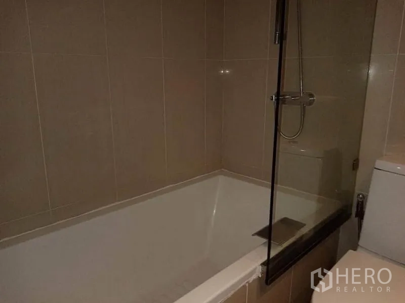Condominium for rent in Sathon, Bangkok - Bathroom with deep bathtub, handheld shower and glass screen.