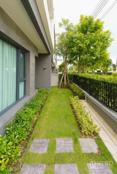 独立式住宅 出租或出售在Bang Phli, Samut Prakan - 房屋侧院草坪与铺石步道，绿篱与乔木。