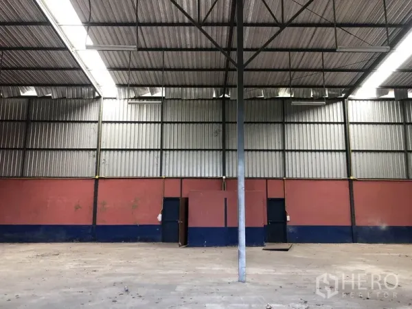 Warehouse for rent in Lam Luk Ka, Pathum Thani - Empty warehouse interior with high steel truss roof, corrugated metal walls, concrete floor and service doors.