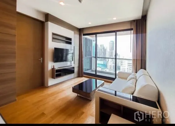 Condominium for rent in Bang Rak, Bangkok - Bright living room with sofa, TV wall and floor-to-ceiling windows opening to a city-view balcony.