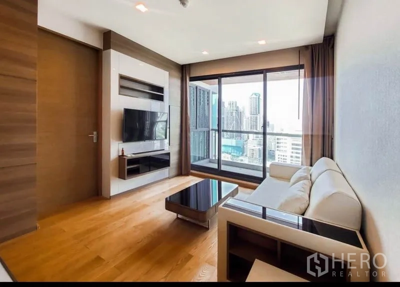 Condominium for rent in Bang Rak, Bangkok - Bright living room with sofa, TV wall and floor-to-ceiling windows opening to a city-view balcony.