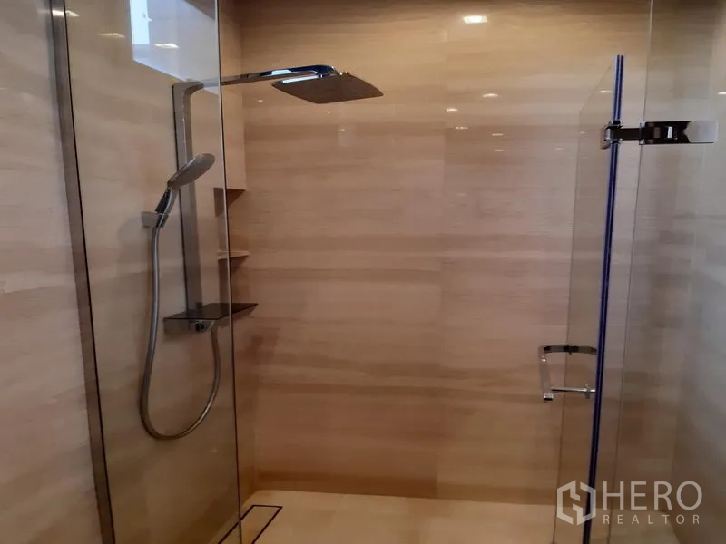 Condominium for rent in Watthana, Bangkok - Glass-enclosed bathroom with rain shower and handheld spray on beige tiles.
