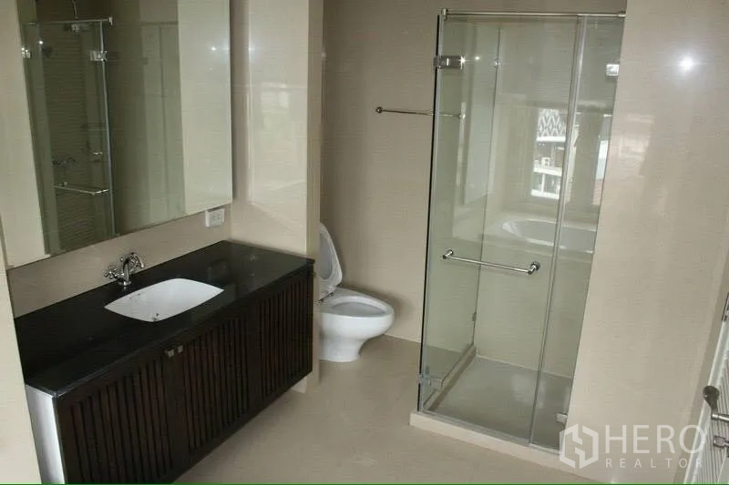 Condominium for rent in Watthana, Bangkok - Modern bathroom with glass-enclosed shower, wide mirror, black countertop vanity, and toilet.