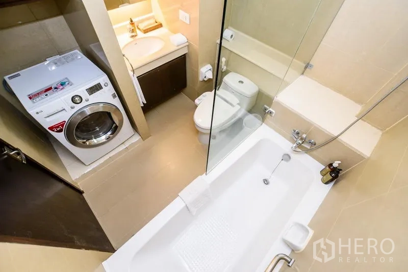 Condominium for rent in Khlong Toei, Bangkok - Bathroom featuring a bathtub with glass screen, vanity, toilet and an in-unit washing machine.