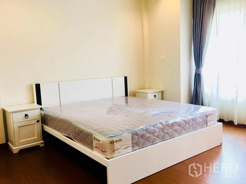 联排别墅 出租在Prawet, Bangkok - 第二卧室配大床与床头柜，窗户配窗帘，木地板。