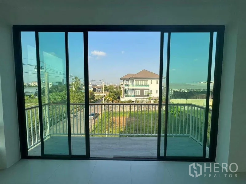 Home Office for rent in Don Mueang, Bangkok - Balcony view through sliding glass doors overlooking a quiet street and houses.