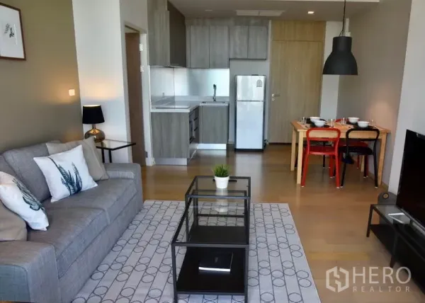 Condominium for rent in Phaya Thai, Bangkok - Open-plan lounge with modern kitchenette, fridge, and a dining set on light wood floors in a Bangkok condo.