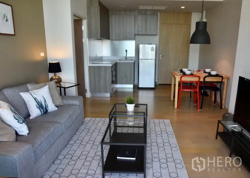 Condominium for rent in Phaya Thai, Bangkok - Open-plan lounge with modern kitchenette, fridge, and a dining set on light wood floors in a Bangkok condo.