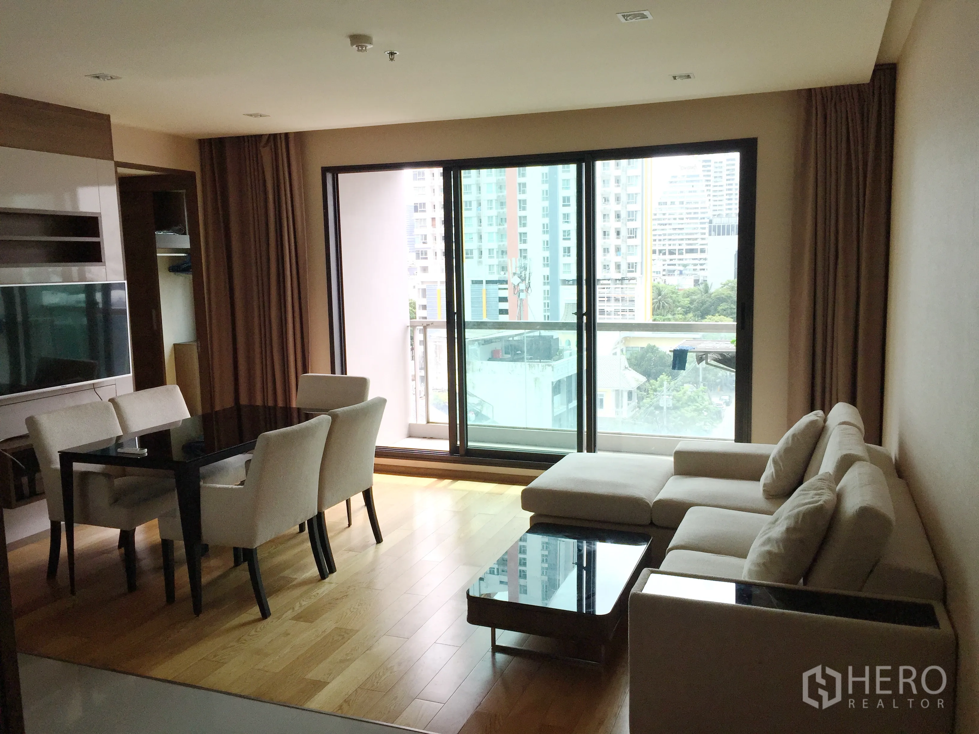 Condominium for rent in Bang Rak, Bangkok - Open-plan living and dining area with L-shaped sofa, four-seat table and a balcony overlooking the city.