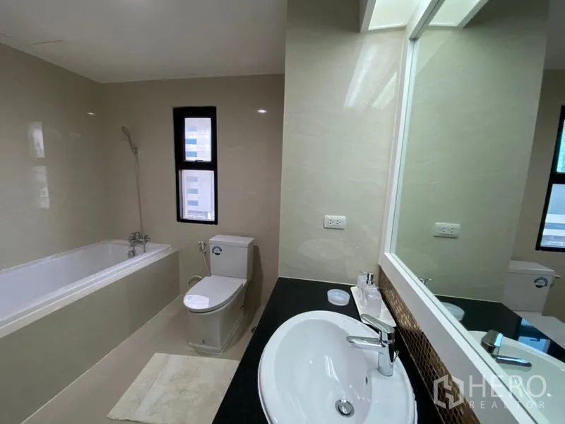 Condominium for rent in Watthana, Bangkok - Modern bathroom with bathtub, vanity sink, toilet, and a slim window for natural light.