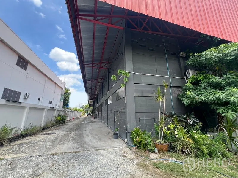 Showroom for rent in Mueang Samut Prakan, Samut Prakan - Side exterior alley with red roof overhang and greenery along building