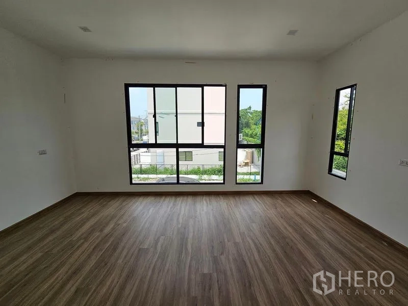Townhouse for rent in Bang Kapi, Bangkok - Spacious corner bedroom featuring multiple black-frame windows, wood flooring and garden views.