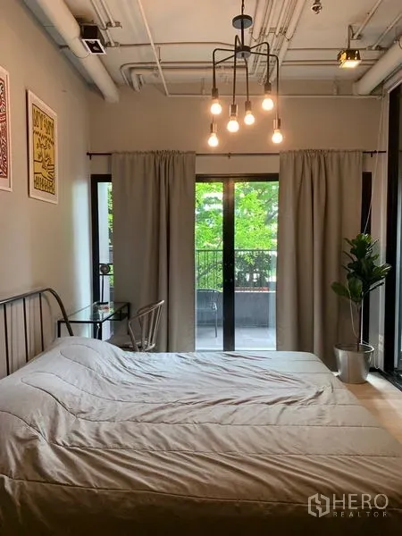 คอนโด ขายในWatthana, Bangkok - ห้องนอนอบอุ่น เพดานโชว์ท่อและโคมไฟ กลางห้องมีประตูกระจกบานเลื่อนออกสู่ระเบียง พร้อมผ้าม่านและกระถางต้นไม้