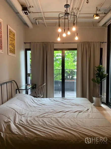 คอนโด ขายในWatthana, Bangkok - ห้องนอนอบอุ่น เพดานโชว์ท่อและโคมไฟ กลางห้องมีประตูกระจกบานเลื่อนออกสู่ระเบียง พร้อมผ้าม่านและกระถางต้นไม้