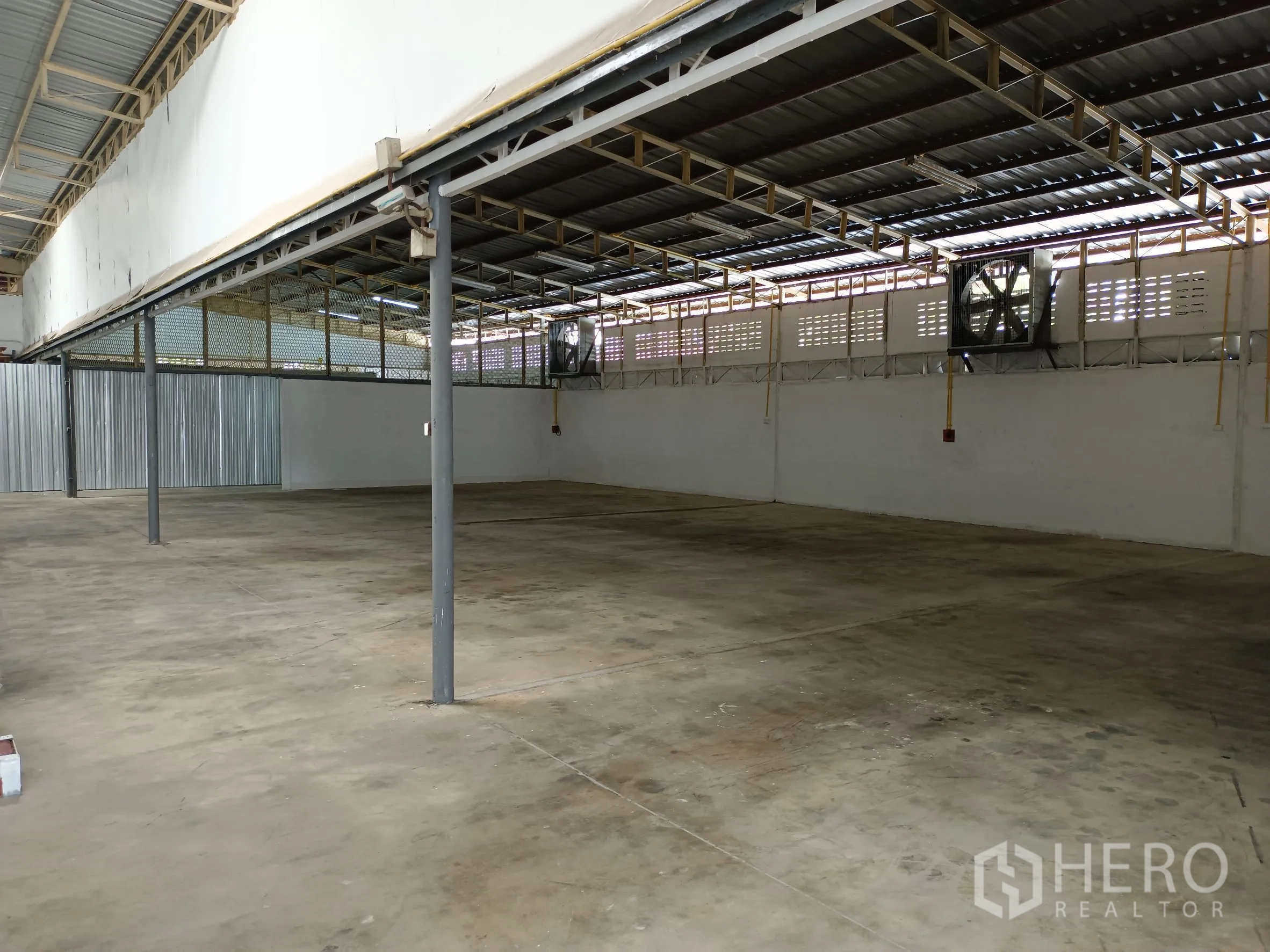 Warehouse for rent in Suan Luang, Bangkok - Spacious storage hall featuring ventilation fans, metal columns and a corrugated partition wall.
