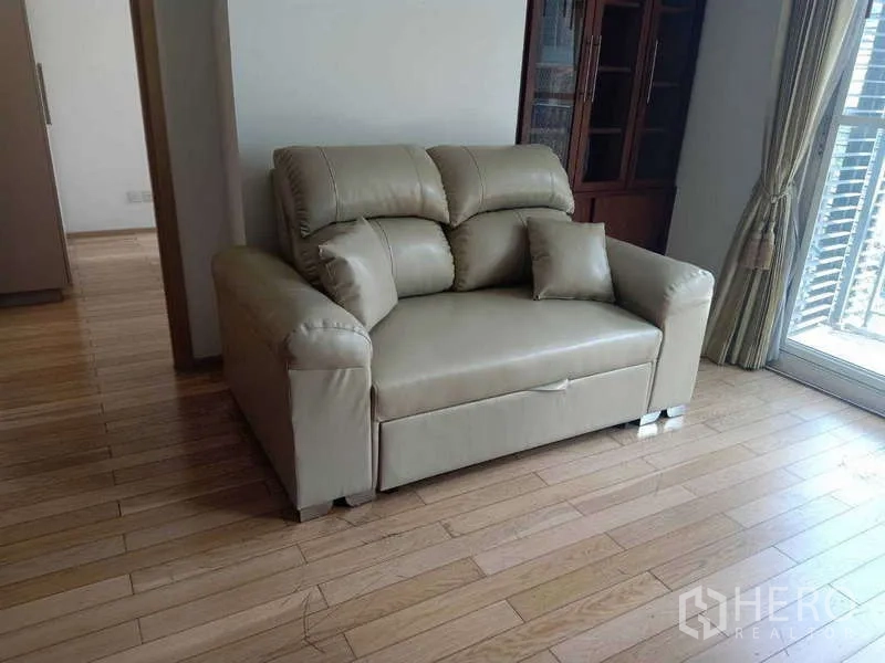 Condominium for rent in Khlong Toei, Bangkok - Leather loveseat in the living area on wood flooring beside the balcony door.
