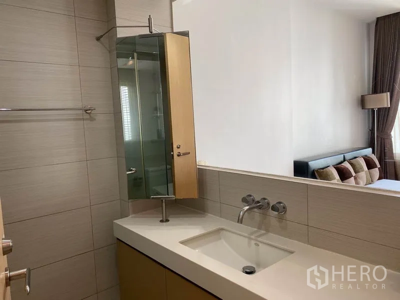 Condominium for rent in Khlong Toei, Bangkok - Sleek bathroom with integrated vanity, wall-mounted faucet and glass partition to bedroom.