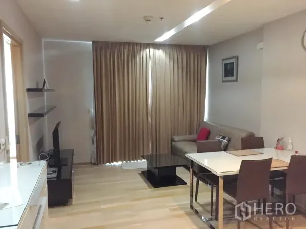 Condominium for rent in Khlong Toei, Bangkok - Cozy living area with sofa, TV console, dining set, and floor-to-ceiling blackout curtains.
