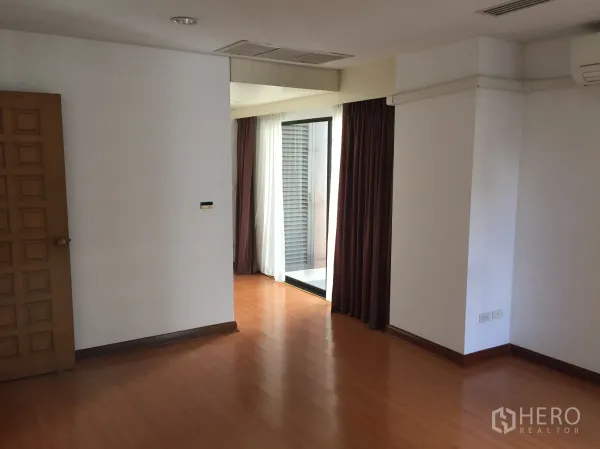 公寓 出租在Pathum Wan, Bangkok - 木地板房间，配空调与通往阳台的推拉玻璃门及窗帘。