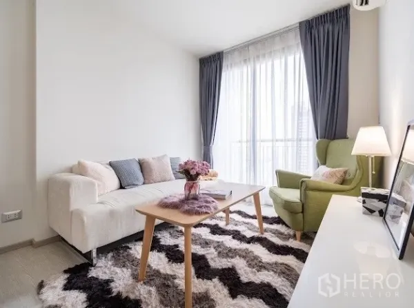 Condominium for sale in Khlong Toei, Bangkok - Cozy living room with floor‑to‑ceiling window, sheer curtains, sofa, green armchair, and balcony view.