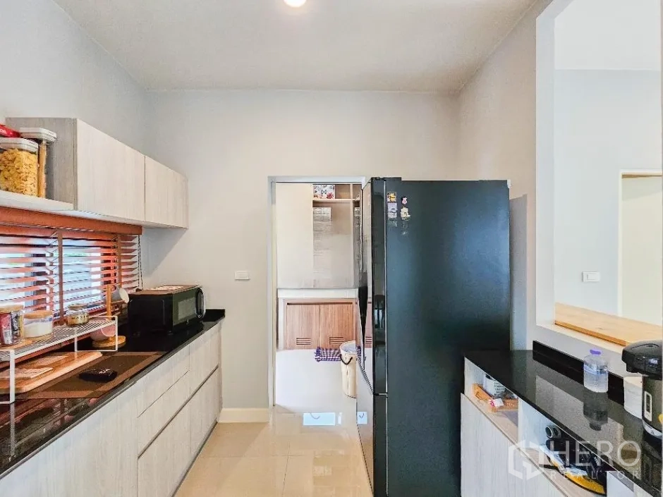 Detached House for sale in Lam Luk Ka, Pathum Thani - Main kitchen with black countertops, tall refrigerator and ample cabinetry.