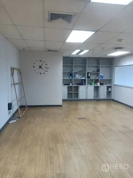 Office Space for rent - Open-plan office area featuring built-in shelving and cabinets, wall clock, fluorescent ceiling lights and wooden floor.