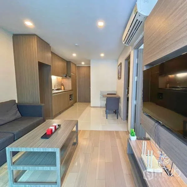 Condominium for rent - TV wall unit and sofa in a wood-floored living room with balcony access.