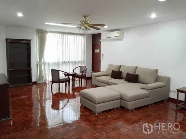 Condominium for rent in Watthana, Bangkok - Large living room with L-shaped sofa, ceiling fan and polished wood floors.