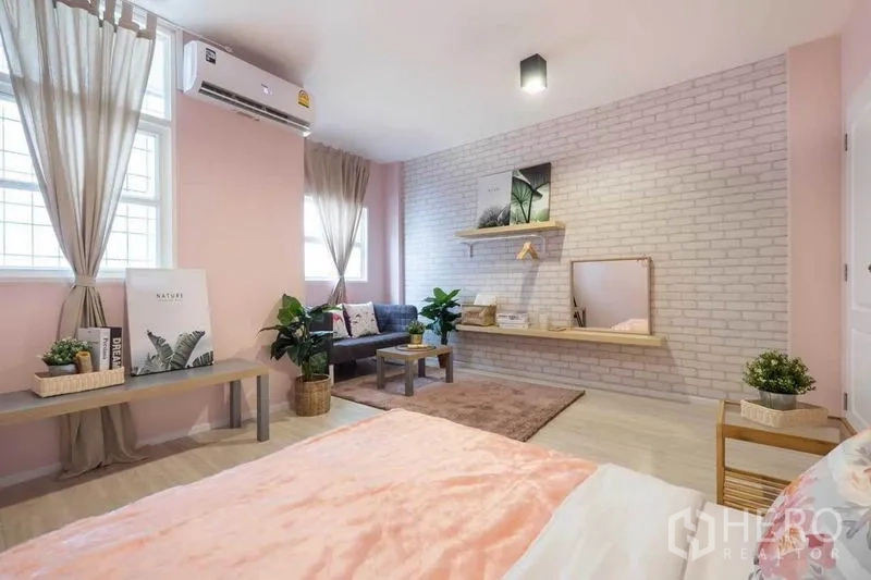 Detached House for rent in Khlong Toei, Bangkok - Spacious pink bedroom with brick feature wall, sofa seating and floating shelf with mirror.