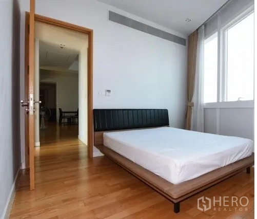 Condominium for rent in Khlong Toei, Bangkok - Cozy secondary bedroom with a platform bed, wood flooring, and a large window with curtains.