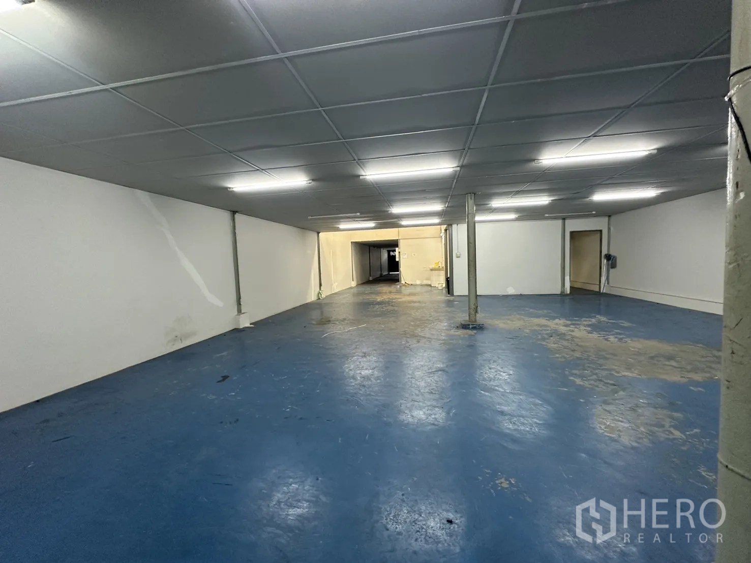 Warehouse for rent in Suan Luang, Bangkok - Large warehouse bay with blue epoxy floor, low ceiling and fluorescent lighting.