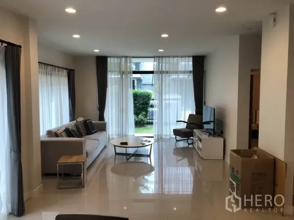 Detached House for rent in Bang Kapi, Bangkok - Bright living room with floor-to-ceiling windows, sofa and TV opening to a small garden.