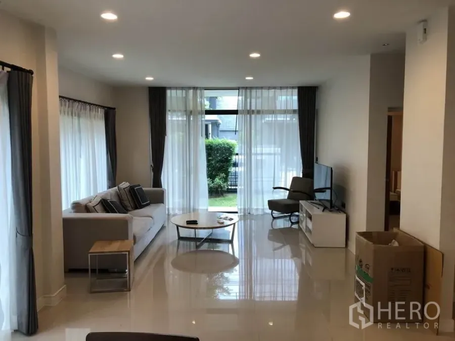 Detached House for rent in Bang Kapi, Bangkok - Bright living room with floor-to-ceiling windows, sofa and TV opening to a small garden.