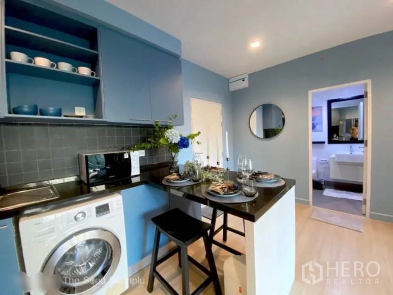 Condominium for rent or sale in Sathon, Bangkok - Compact kitchen with blue cabinetry, breakfast bar and in‑unit washer.