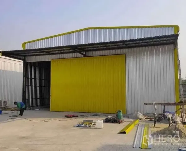 Warehouse for rent in Khlong Sam Wa, Bangkok - Metal-clad warehouse with bright yellow sliding door and loading canopy on a concrete yard in Khlong Sam Wa, Bangkok.
