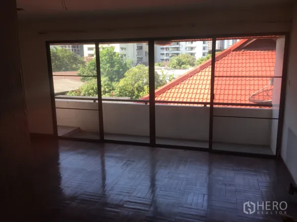 带办公室的家 出售在Watthana, Bangkok - 房间连接阳台，落地窗外见红瓦屋顶与树景。