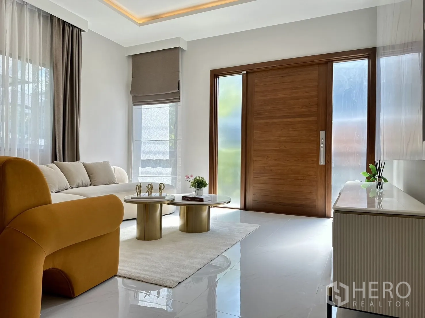Detached House for rent or sale - Sunlit lounge with large wooden front door, sectional sofa, gold coffee tables and recessed ceiling lighting.