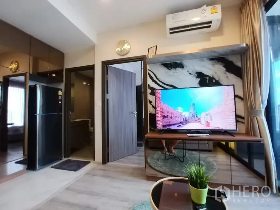 公寓 出租在Huai Khwang, Bangkok - 客厅设有大理石纹背景墙、电视与空调，旁有通往卧室与浴室的门。