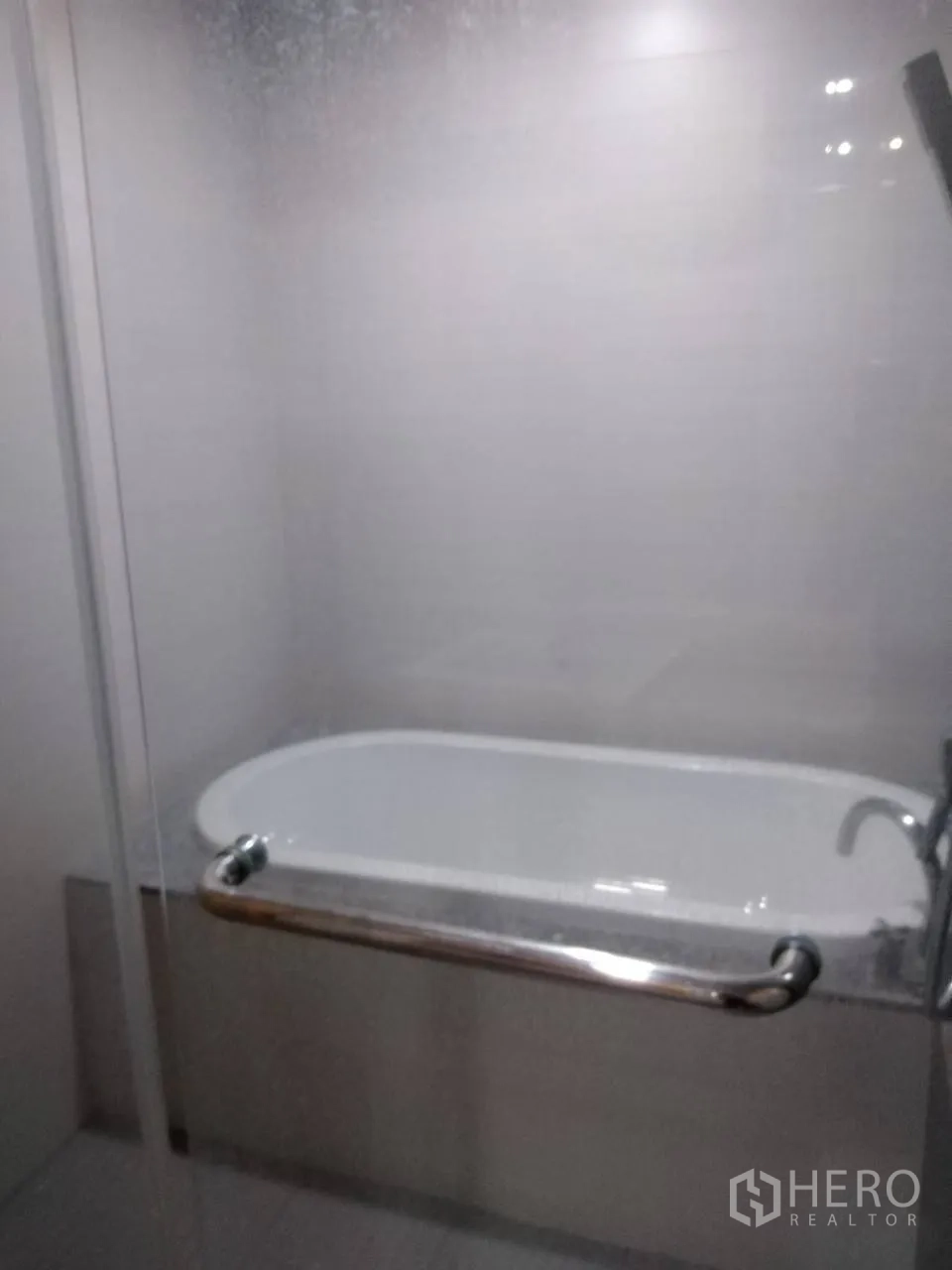 Condominium for rent in Khlong Toei, Bangkok - Bathtub with glass screen and safety grab bar inside a tiled bathroom.