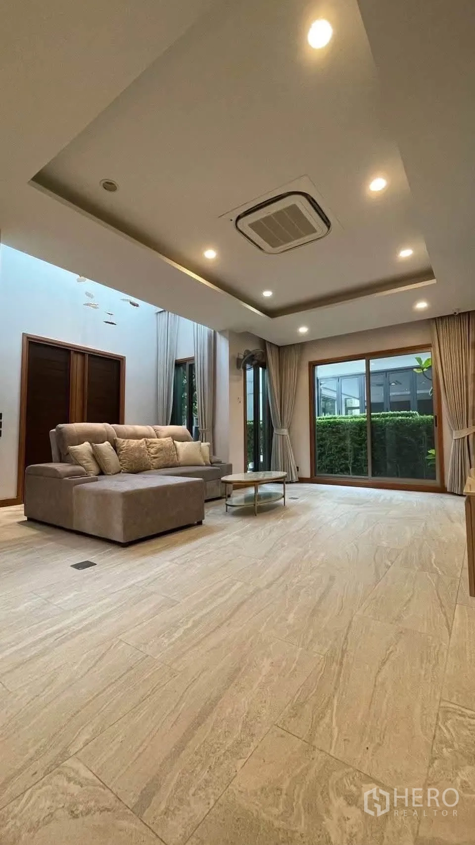Detached House for rent in Prawet, Bangkok - Living room with L-shaped sofa, coffee table and sliding doors to hedge garden.