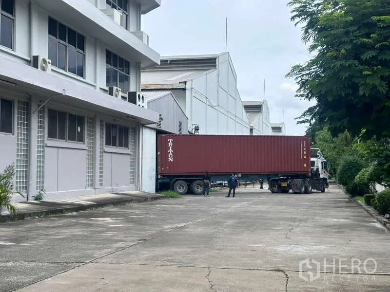 Warehouse for rent in Mueang Samut Prakan, Samut Prakan - Container truck at warehouse loading dock with wide driveway and greenery in Samut Prakan.