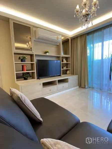 Condominium for rent in Bang Rak, Bangkok - Bright living room with built-in TV wall, chandelier and sheer curtains opening to the balcony.
