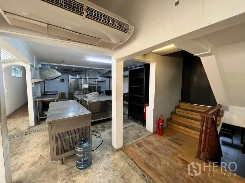 Retail Space for rent in Bangkok - Back-of-house prep area with stainless tables, stairs and air-conditioning unit.