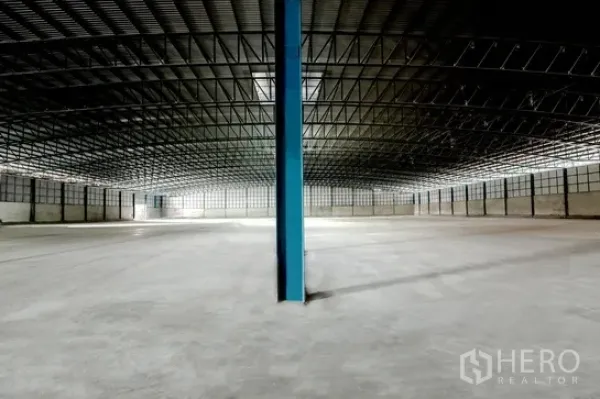 货栈 出租在Pathum Thani - 开放式仓库空间，中央蓝色立柱与周边通风玻璃砖墙。