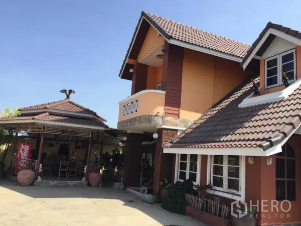 Detached House for rent or sale in Bang Bua Thong, Nonthaburi - Angle view of the house with a covered outdoor pavilion beside a wide paved courtyard.