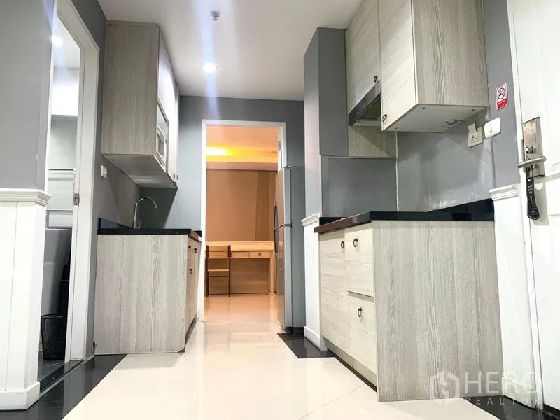 Condominium for rent in Khlong Toei, Bangkok - Galley layout with dual kitchen counters and light wood cabinetry leading to bedrooms.