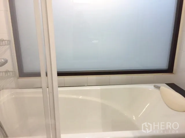 Condominium for rent or sale in Khlong Toei, Bangkok - Bright bathroom with full-size bathtub beside a frosted glass window and sliding shower screen.
