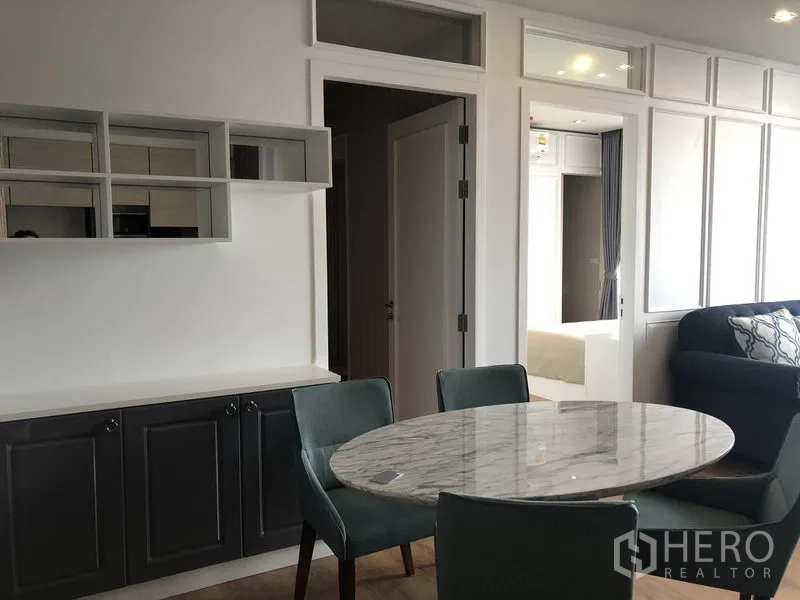 Condominium for rent in Khlong Toei, Bangkok - Dining corner with round marble table, teal chairs, and built-in cabinets.