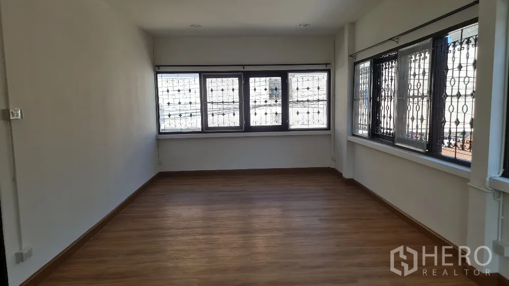 Detached House for rent in Lat Phrao, Bangkok - Sunlit bedroom with wood floors and windows fitted with security grilles.